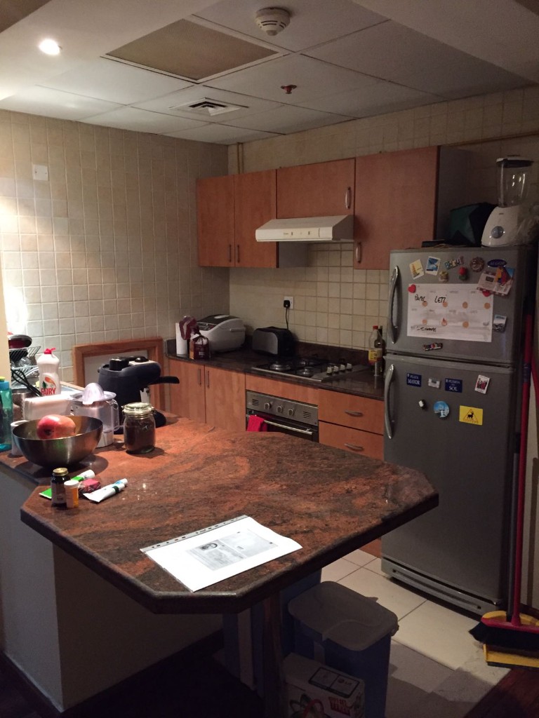 Before — dated cluttered kitchen with granite peninsula